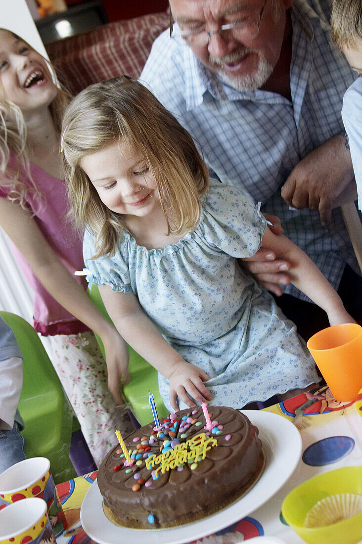 Little girl s third birthday party, looking at her cake with her grandad.