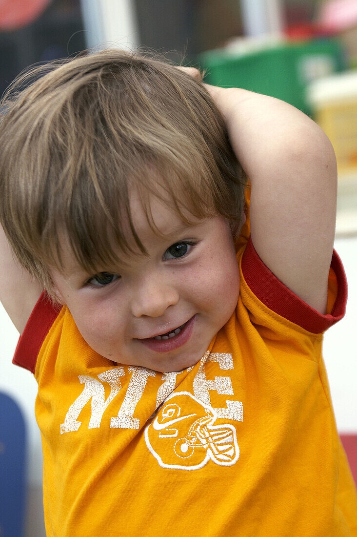 3 year old boy, looking into camera, at nursery, smiling, with his arms above his head