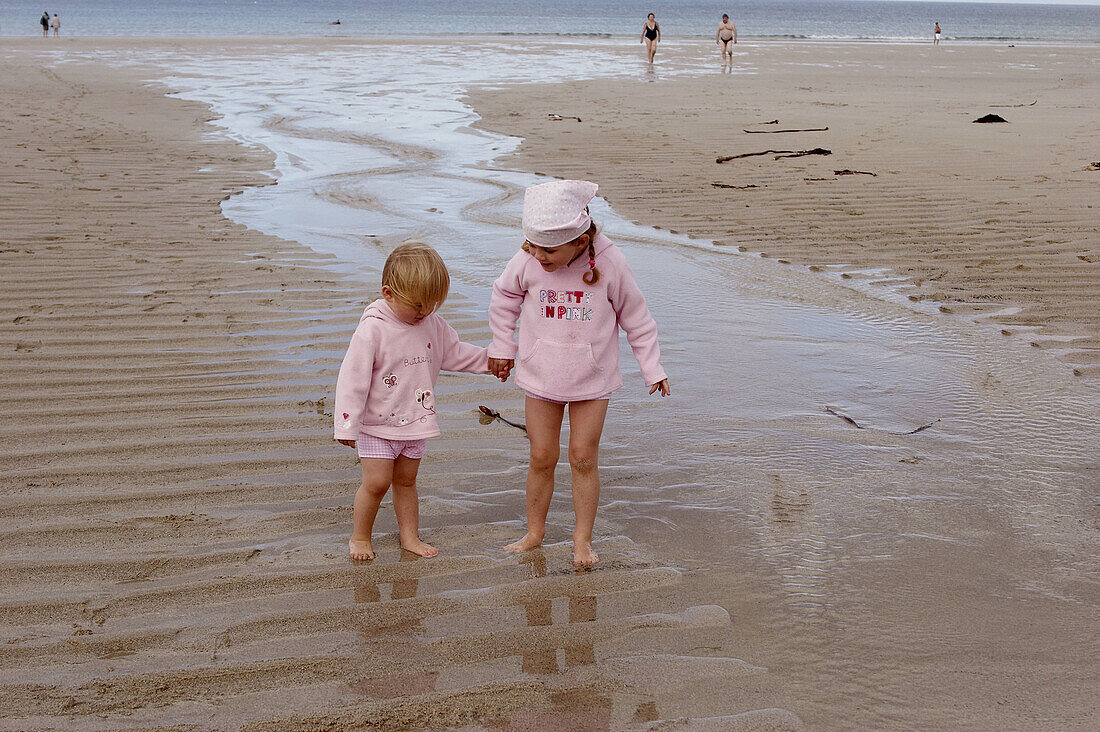 4 and 2 year old girls standing on the beach holding hands, laughing
