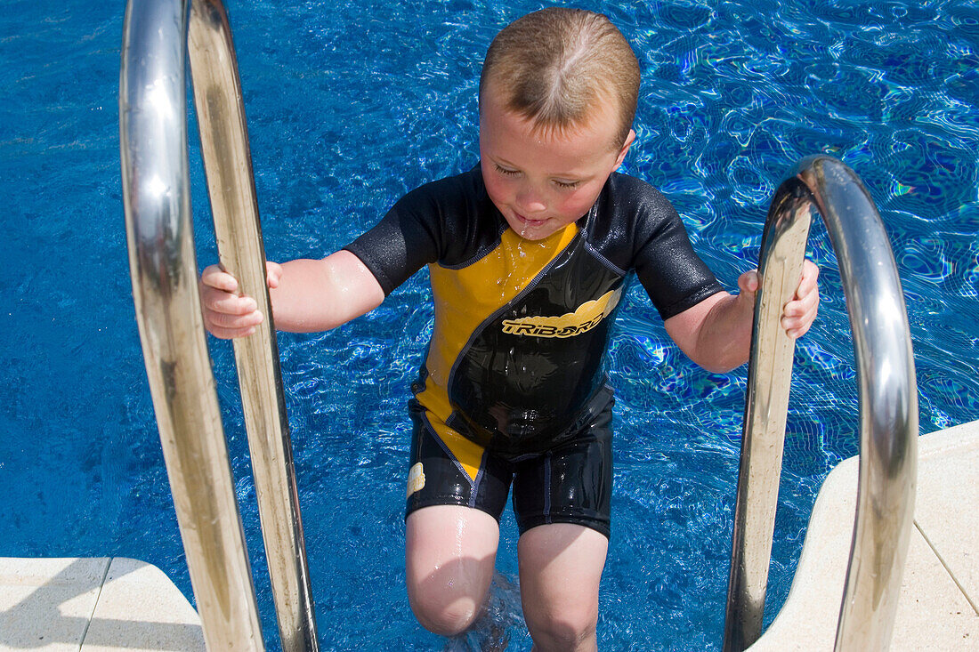 4 year old boy climbing out of the swimming pool; outside, wearing a wetsuit