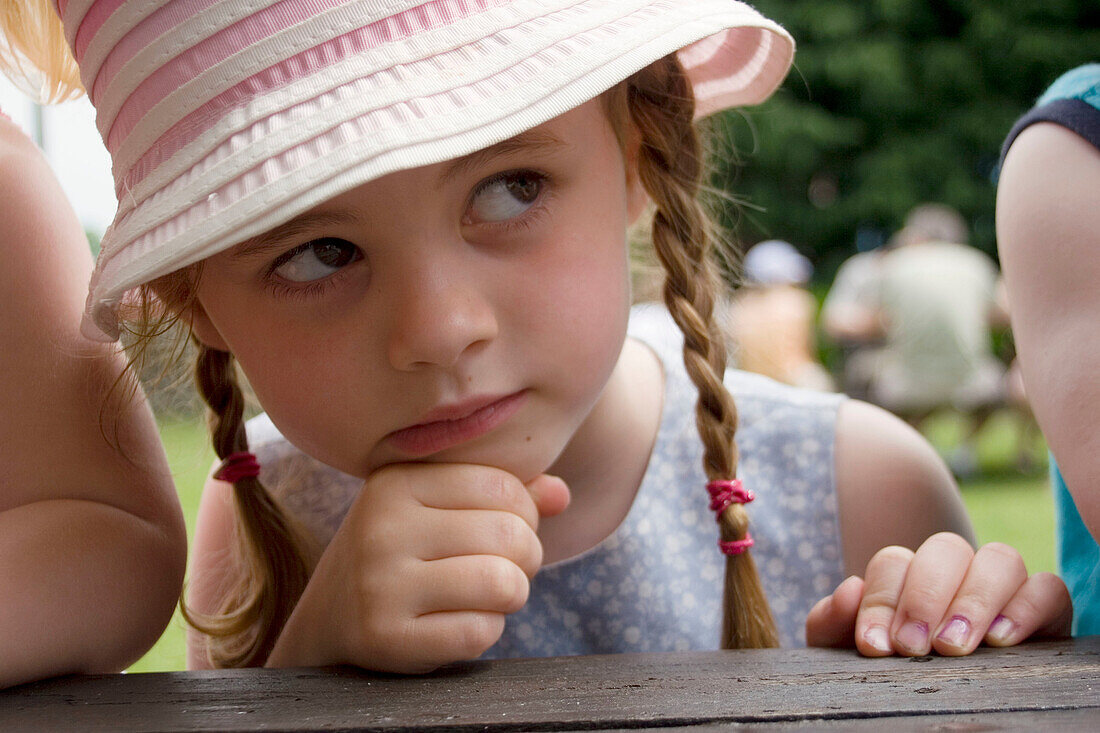 4 year old girl sitting outside with her chin in her hand.