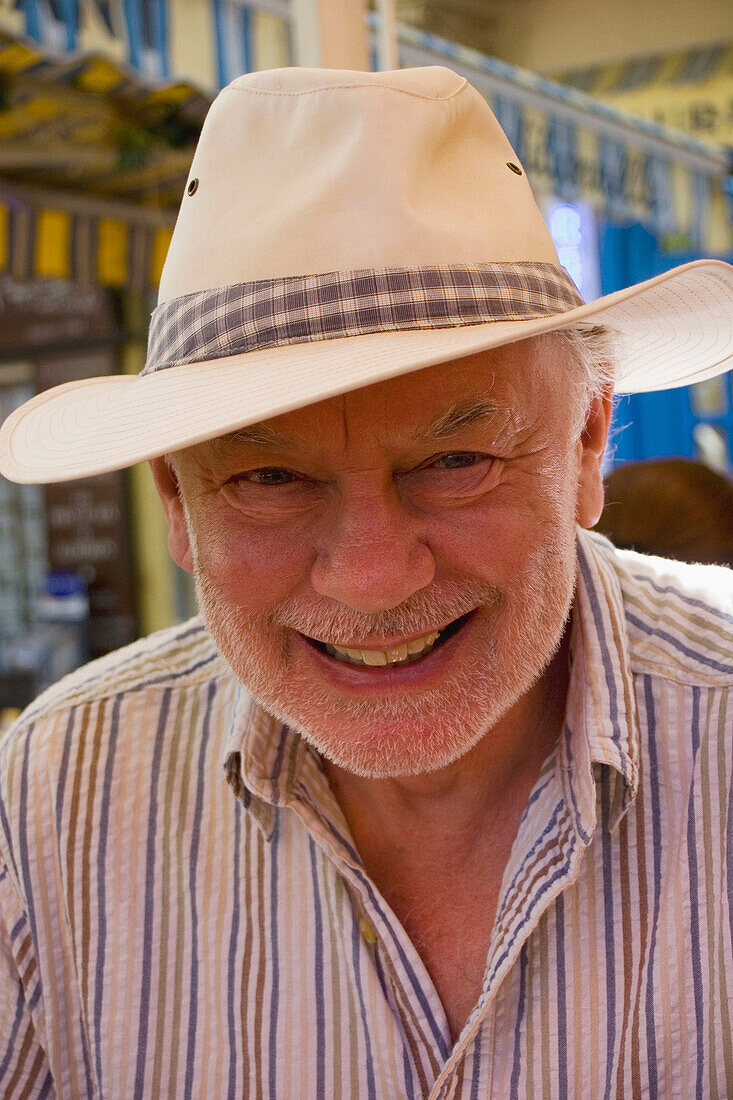 good looking 70 year old man wearing a sunhat, with a grey beard, smiling into camera ,in the sunshine