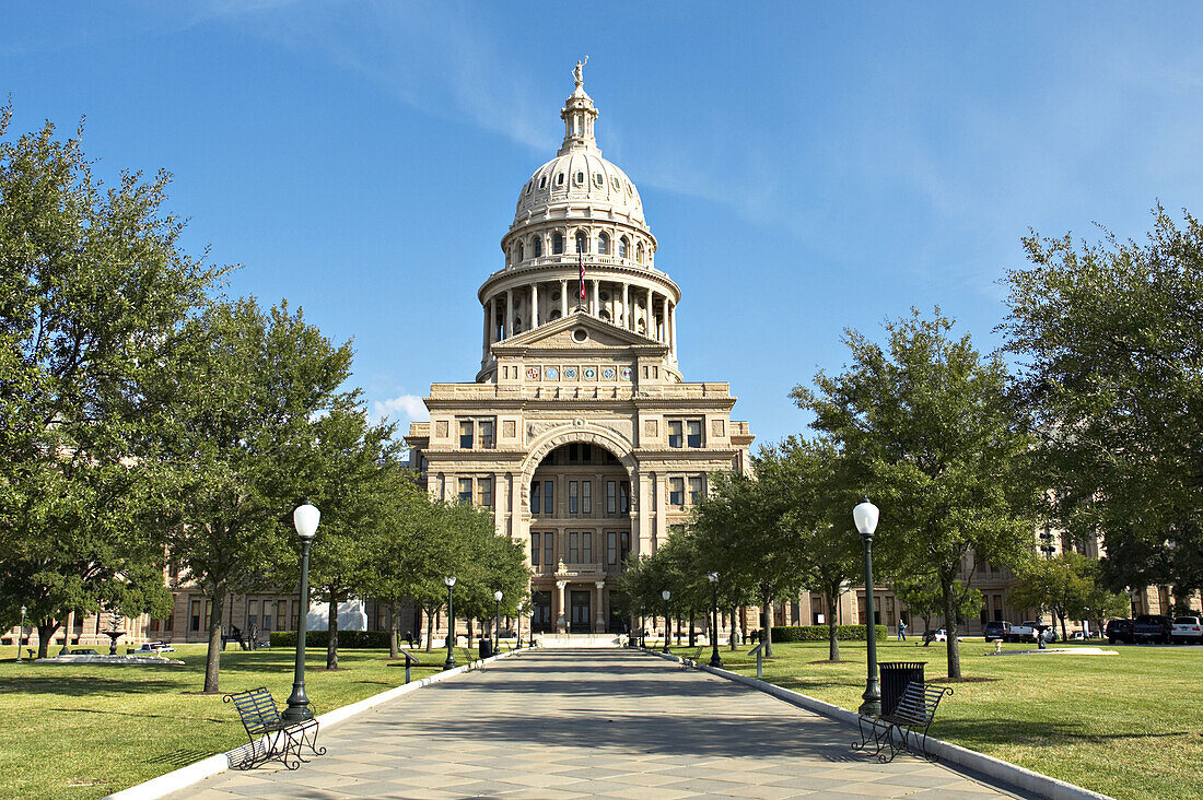 Texas, Austin. Goddess of Liberty hold star atop dome of state capitol building, green space around building, trees, street lamps along sidewalk