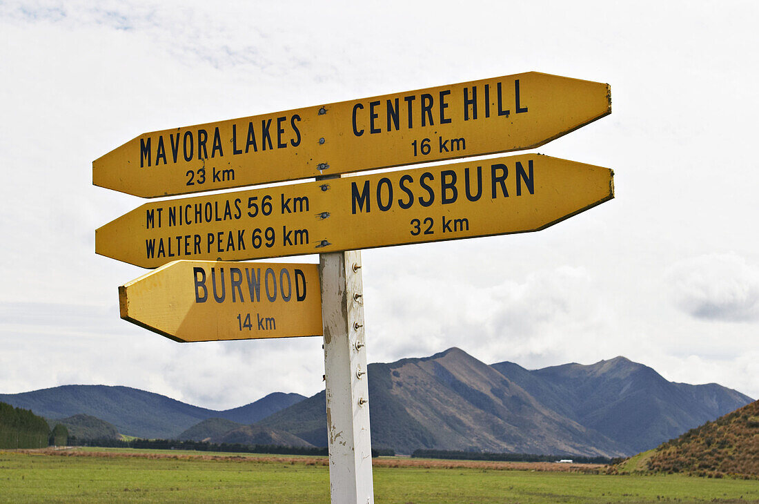 New Zealand. South Island. Signpost with yellow arrows, distance in kilometers to various towns and locations, Movara Lakes, Burwood, Mossburn, Walter Peak, Mt. Nicholas, Centre Hill