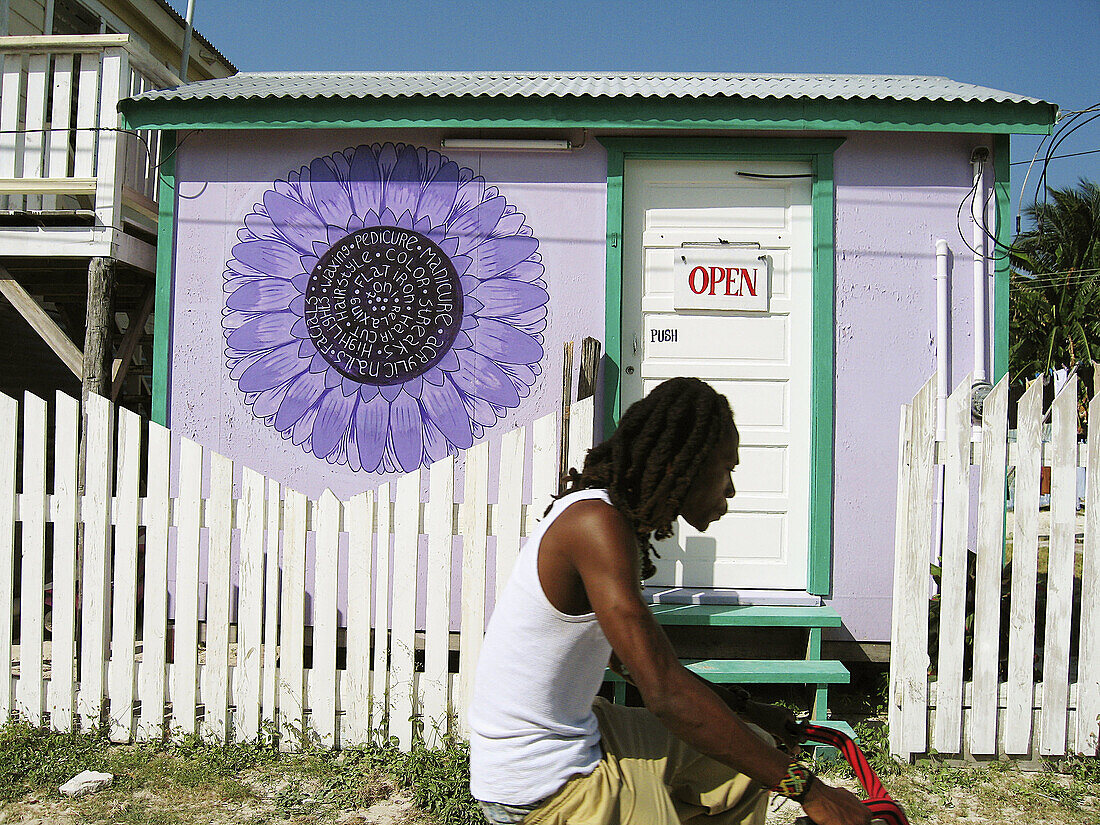 BELIZE Caye Caulker Open sign on white door, small purple building for spa, white picket fence, man bicycle past