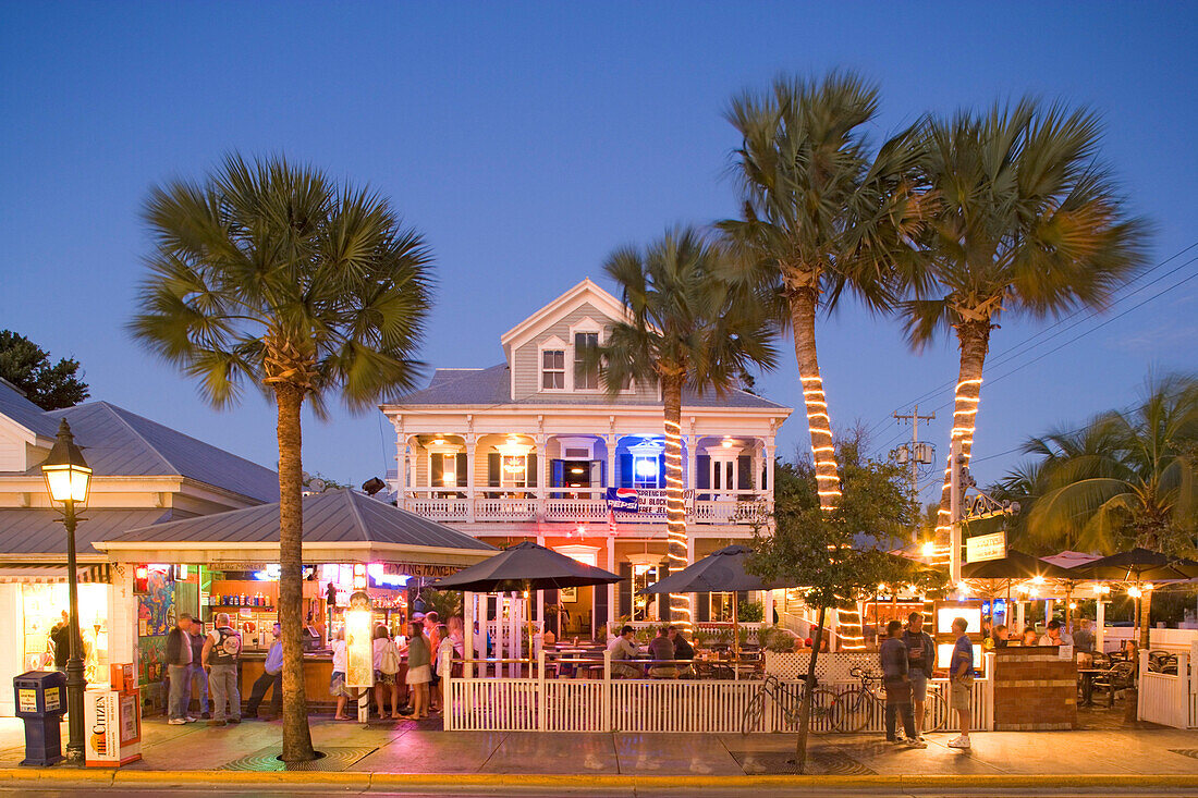 Menschen sitzen abends auf der beleuchteten Terrasse einer Bar, Duval Street, Key West, Florida Keys, Florida, USA