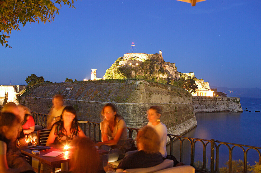 Menschen sitzen abends im Café Aktaion, im Hintergrund die alte Festung, Korfu, Ionische Inseln, Griechenland