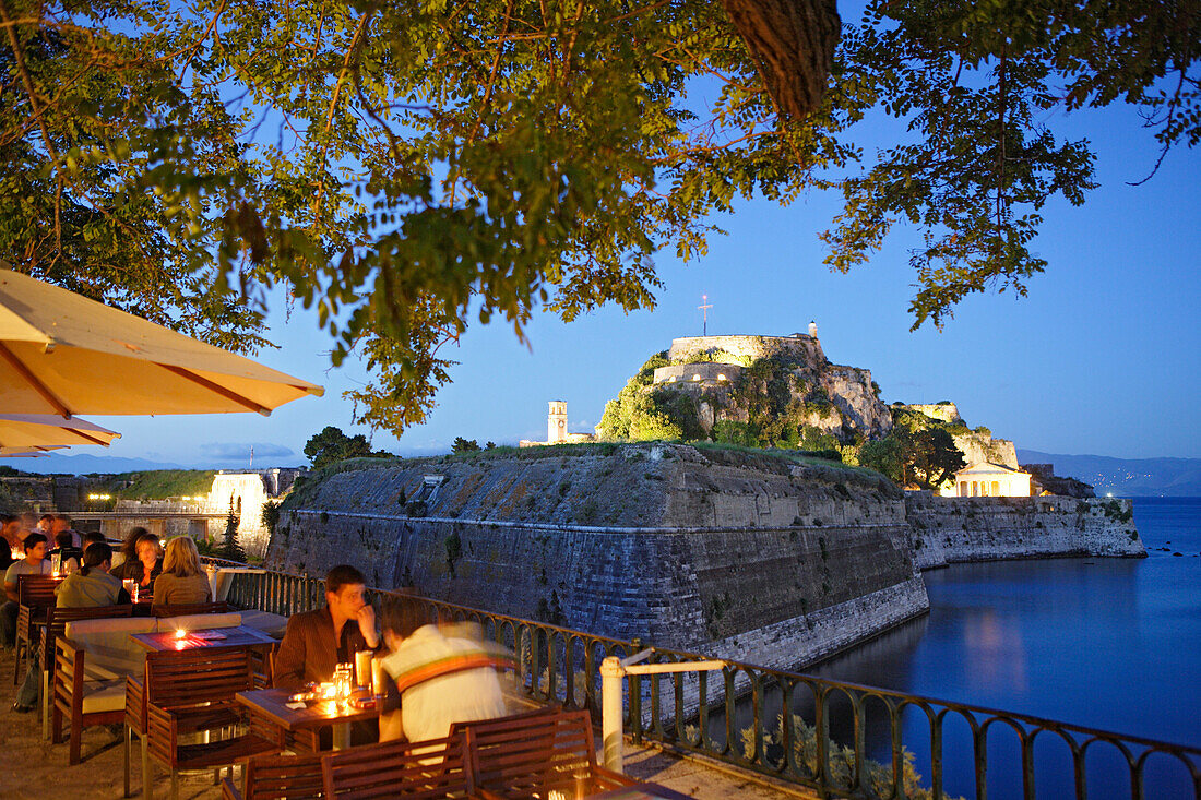 Menschen sitzen abends im Café Akteion, im Hintergrund die alte Festung, Korfu, Ionische Inseln, Griechenland