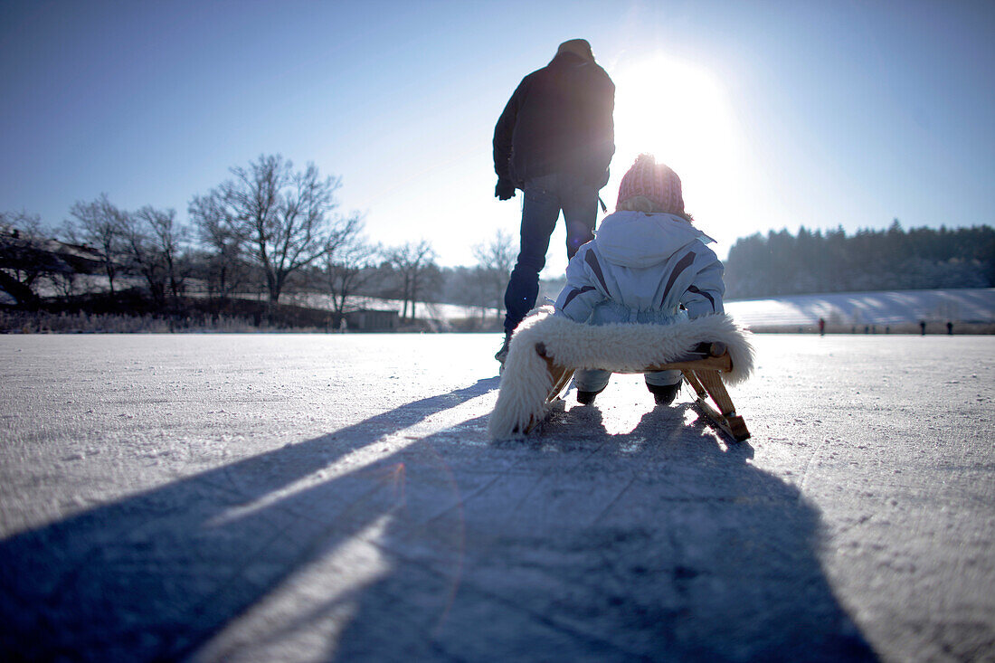 Vater zieht Kind auf einem Schlitten über den Buchsee, Münsing, Bayern, Deutschland