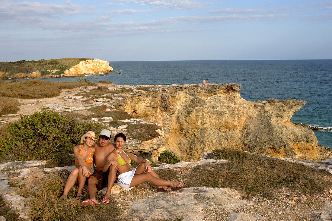 Zwei Frauen und ein Mann sitzen lächelnd auf Felsen an der Küste, Cabo Rojo, Puerto Rico, Karibik, Amerika