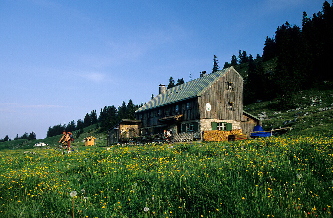 hut Riesenhütte with two mountainbikers, Hochries, Chiemgau range, Chiemgau, Bavarian foothills, Upper Bavaria, Bavaria, Germany