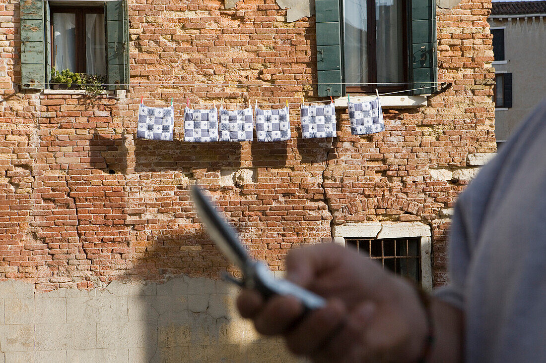 Man with mobile phone, washing line with drying pillows hung on a building, Venice, Veneto, Italy