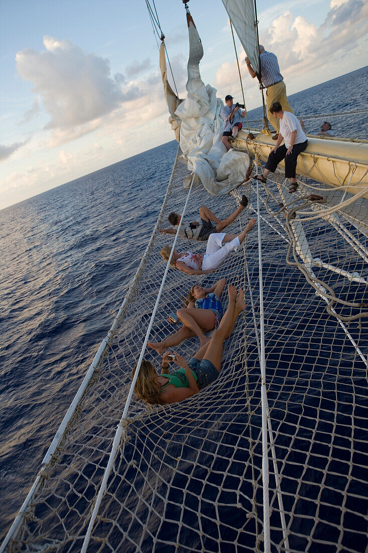 Passagiere entspannen sich im Bugspriet Netz vom Großsegler Star Flyer, Rangiroa, Tuamotu Inseln, Französisch Polynesien, Südsee