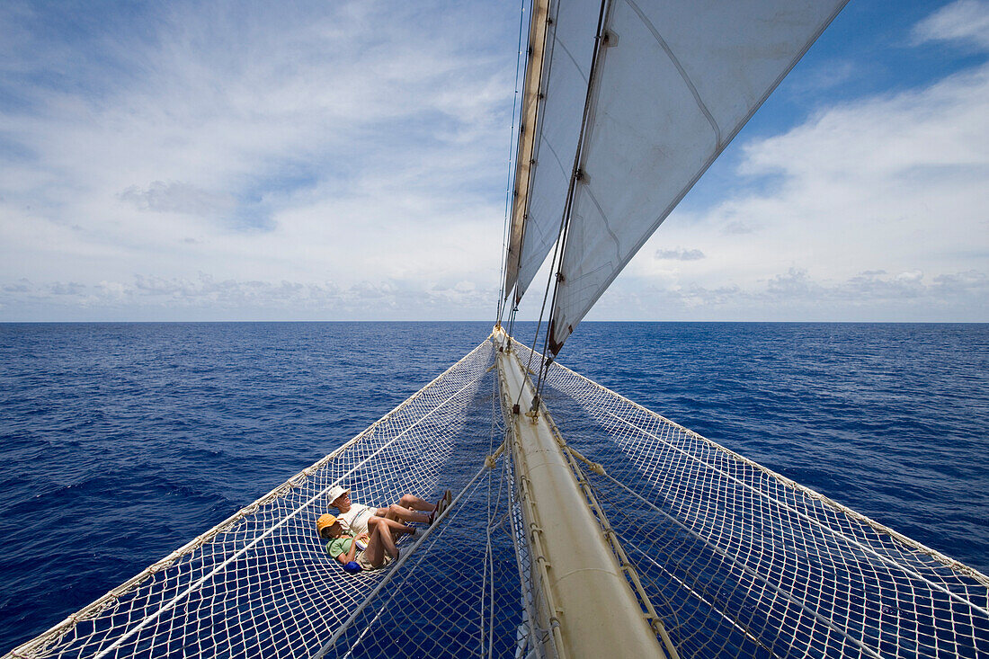 Couple relaxing in bowsprit net of sailing Cruiseship Star Flyer (Star Clippers Cruises), Bora Bora, Society Islands, French Polynesia