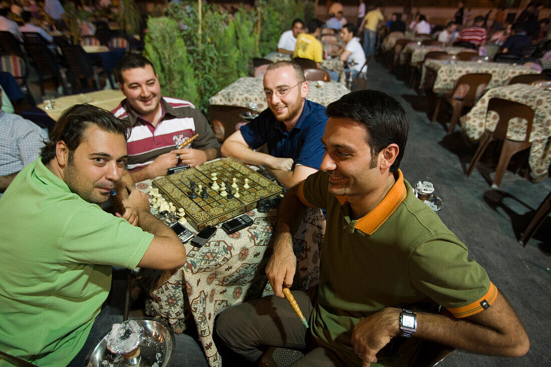 Men playing a game of chess and smoking a Shisha water pipe at an outdoor cafe near the Citadel, Aleppo, Syria, Asia