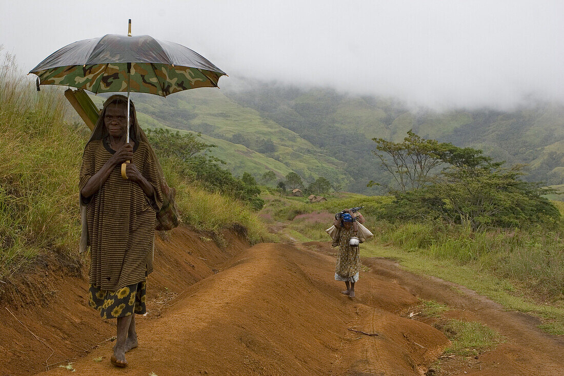 Woman walking with umbrella on track, Langila, Highland, Papua New Guinea, Oceania
