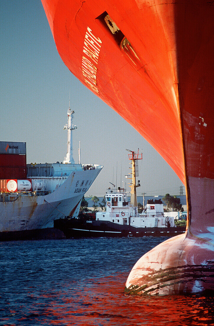 Tugboat and container ship framed by bow of boat in foreground