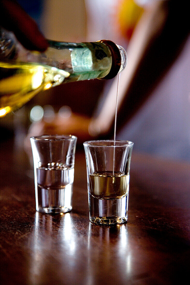 Person pouring Grappa into two glasses, Nardini Grappa Bar, Bassano del Grappa, Veneto, Italy