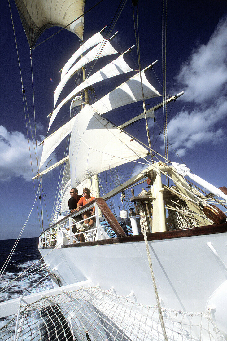 Two passengers leaning by the starboard rail and enjoying the sail as the clipper ship Star Clipper sails along the Yucatan coast towards Honduras