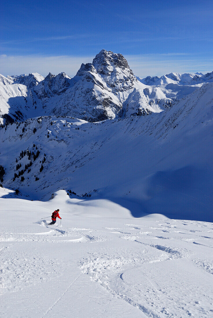 Junge Frau bei Pulverschneeabfahrt von der Güntlespitze, im Hintergrund der Widderstein, Kleinwalsertal, Allgäuer Alpen, Allgäu, Vorarlberg, Österreich