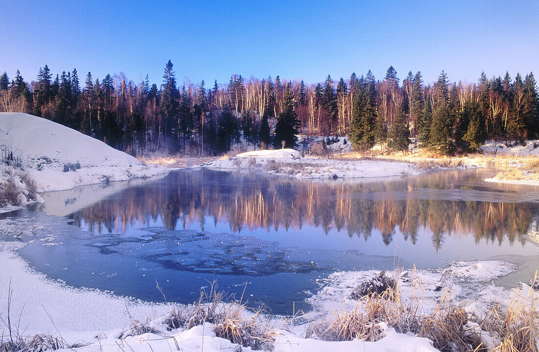 Morning light on snow dusted shore arround open water of Junction creek. Walden. Ontario. Canada 