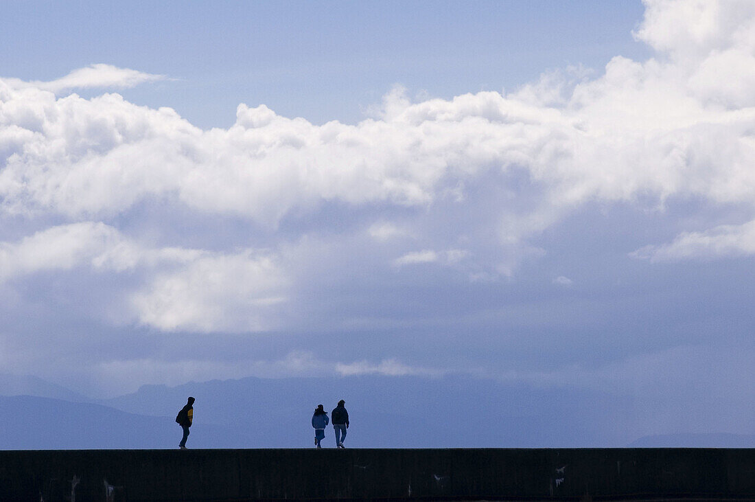 Human figures walking on Victoria breakwater sea wall. Victoria, BC, Canada