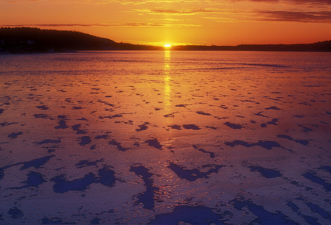 Setting sun, windswept snow and fresh ice on Kelly Lake in early winter. Sudbury. Ontario, Canada