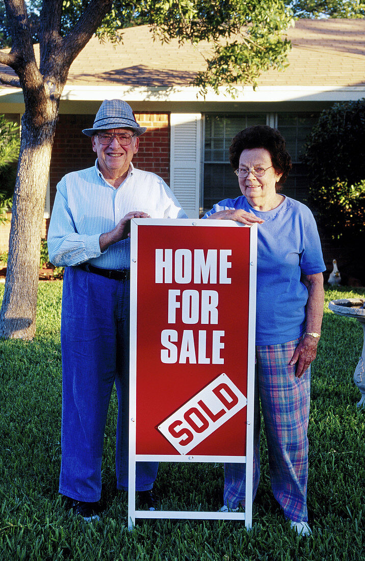 Senior couple in front of home for sale with sign