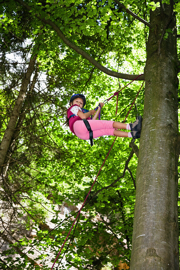 Mädchen (8-9 Jahre) seilt sich von einem Baum ab, Oberbayern, Bayern, Deutschland