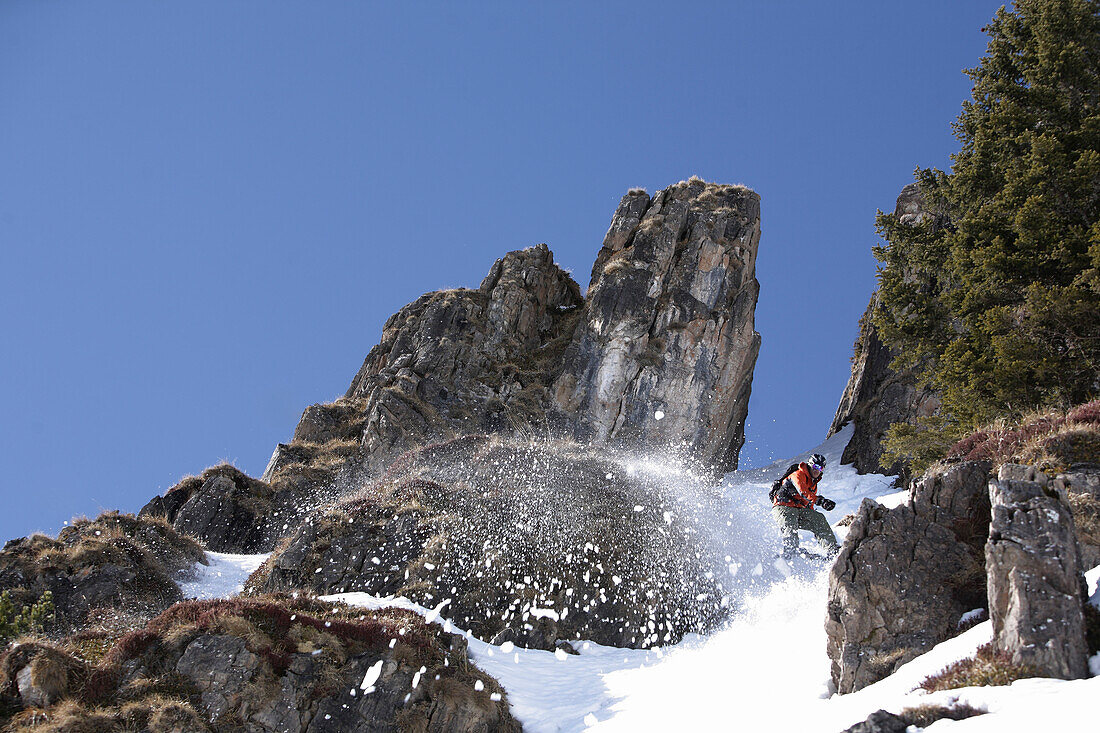 Young man snowboarding between rocks, Fieberbrunn, Tyrol, Austria