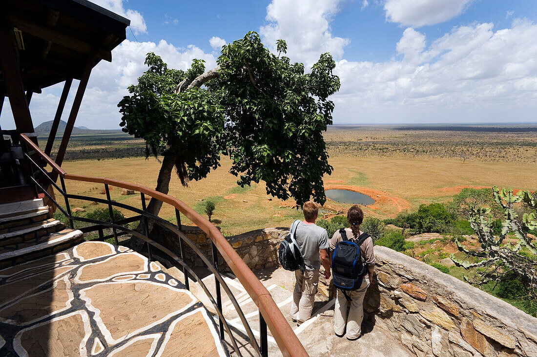 Guests looking over waterhole to savannah, Voi Safari Lodge, Tsavo East National Park, Coast, Kenya