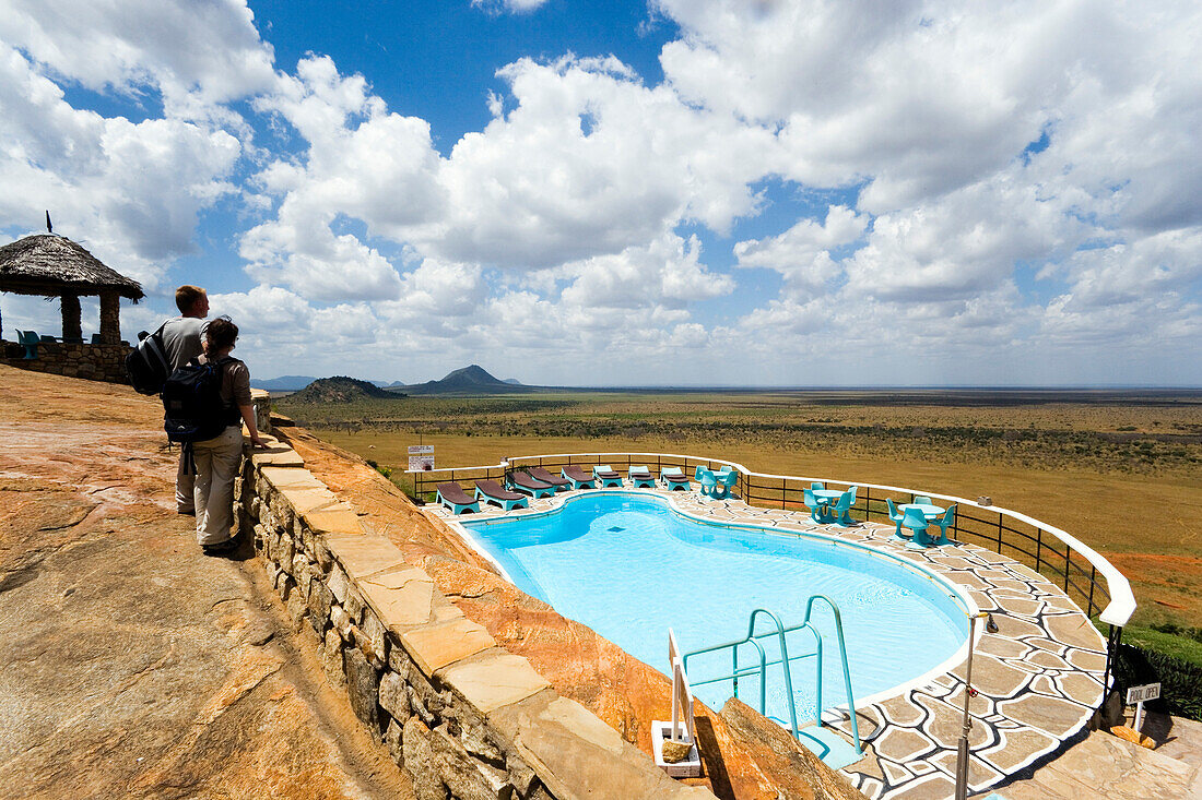 Guests looking over swimming pool to savannah, Voi Safari Lodge, Tsavo East National Park, Coast, Kenya