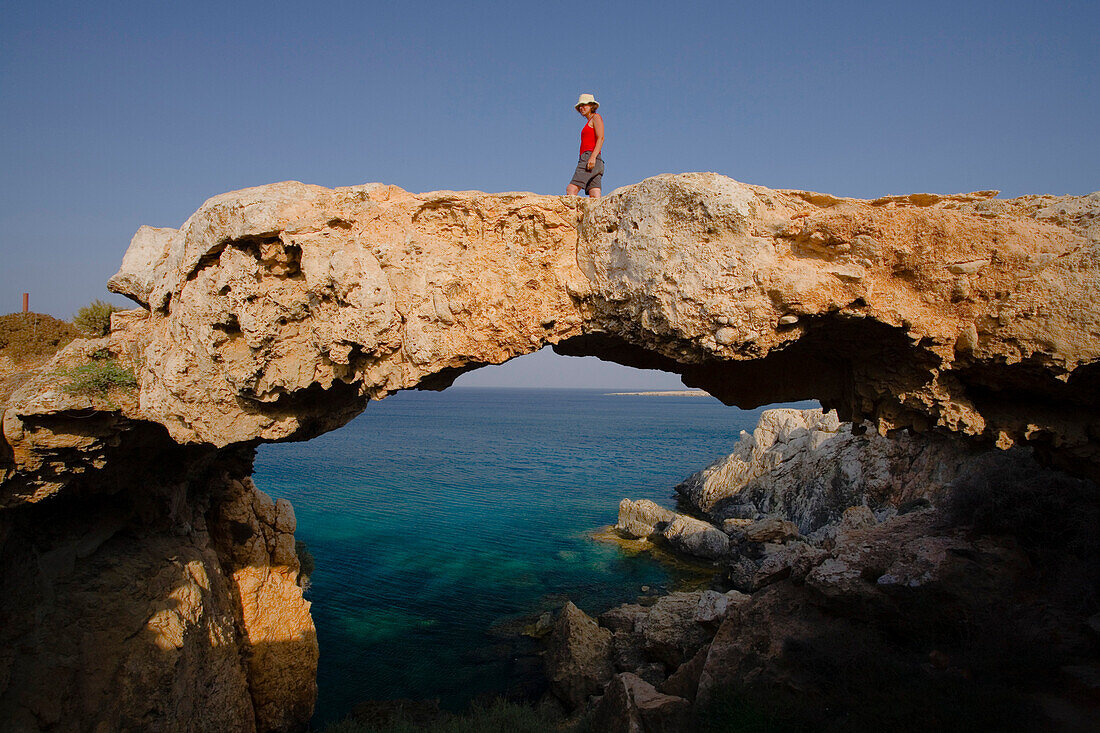Woman walking over a natural bridge, Rocky coastal landscape at Cape Gkreko, near Protaras, near Agia Napa, South Cyprus, Cyprus