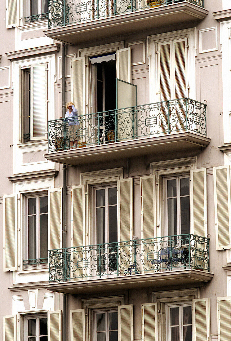 Elderly woman looking out from her balcony. Nice, France