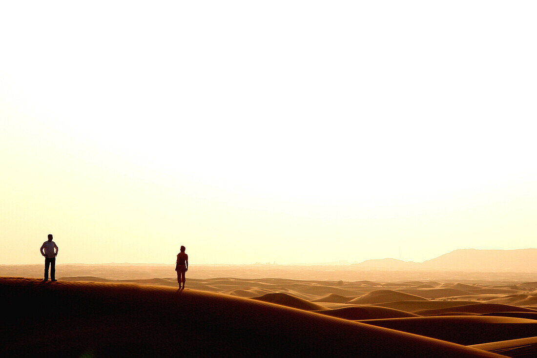 Paar betrachtet Sonnenuntergang in der Wüste, Dubai, Vereinigte Arabische Emirate, VAE