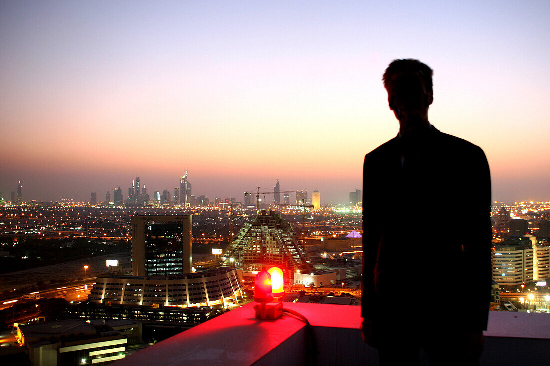 Mann blickt auf abendliches Dubai vom Dach des Grand Hyatt Hotel, Dubai, Vereinigte Arabische Emirate, VAE