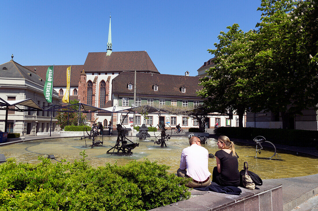 Ein Paar sitzen am Brunnen, Jean Tinguely Brunnen mit maschinenähnlichen Skulpturen, Theaterplatz, Basel, Schweiz