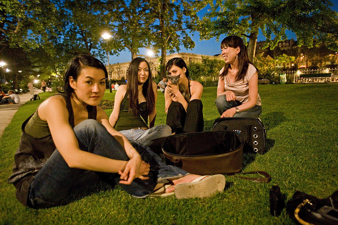 Young japanese women sitting in a meadow at Isle de la Cité at night, Paris, France, Europe