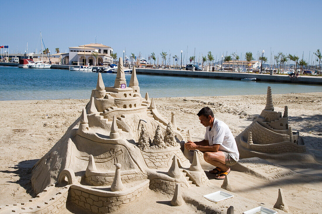 Mann baut Sandburg Skulptur am Strand von Port de Pollenca, Mallorca, Balearen, Spanien, Europa