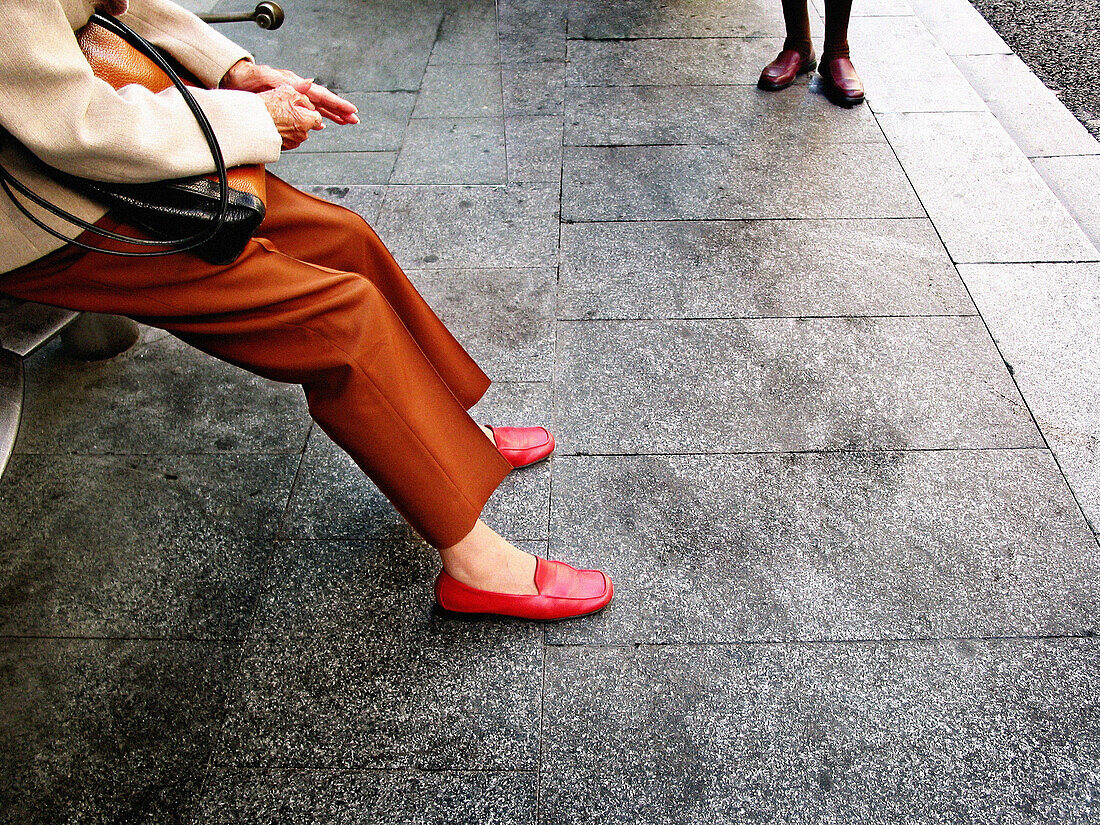 Adult, Adults, Anonymous, Bench, Benches, Color, Colour, Contemporary, Daytime, Exterior, Female, Gray, Grey, Horizontal, Human, Leg, Legs, Outdoor, Outdoors, Outside, Pair, Pavement, Pavements, People, Person, Persons, Seated, Sidewalk, Sidewalks, Sit, S