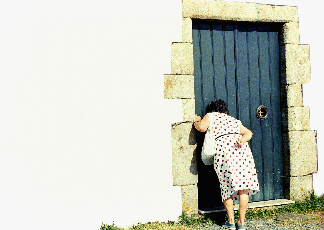 Adult, Adults, Back view, Closed, Color, Colour, Contemporary, Curiosity, Curious, Daytime, Door, Doors, Entrance, Entrances, Entries, Entry, Europe, Exterior, Female, Full-body, Full-length, Galicia, Horizontal, Human, Look, Looking, Mature Adult, Mature