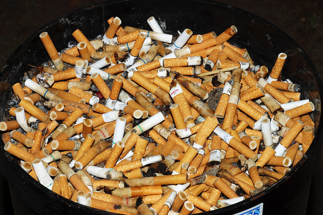A diversity of filter cigarettes as cigarette butts in a huge ashtray in the outdoors in a special allocated smoking space for smokers