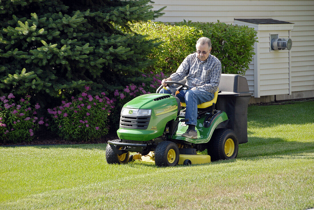 Senior man mows lawn on a riding grass cutting mower