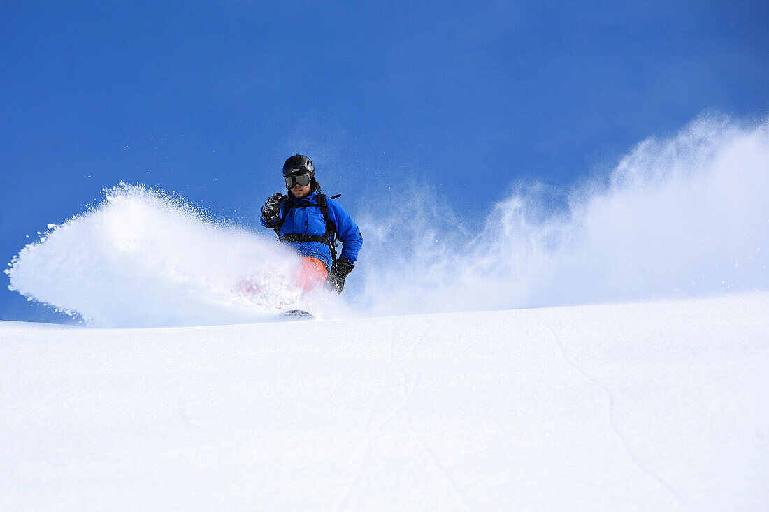 Snowboarder bei der Abfahrt unter blauem Himmel, Skigebiet Paznaun, Tirol, Österreich