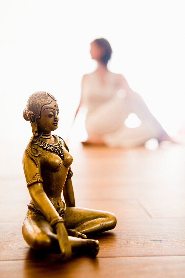 Frau mittleren Alters macht Yoga, Buddhafigur im Vordergrund (Drehsitz), Yogastudio in Linz, Österreich