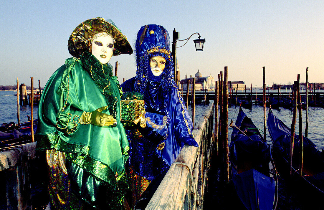 Two people on a small pier over Grand Canal dressed in lavish costumes and masks for the annual masquerade carnival in Venice, Italy