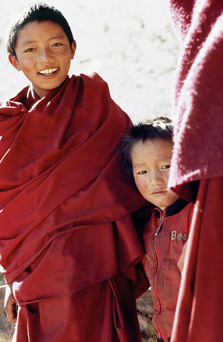 Two very young Tibetan monks hiding behind their older brother also wearing monk clothes. Tibet, China, Asia.