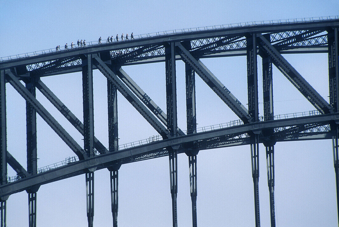 People walking across the top of the Sydney Harbor Bridge on a tourist attraction offered by BridgeClimb, Sydney, Australia.