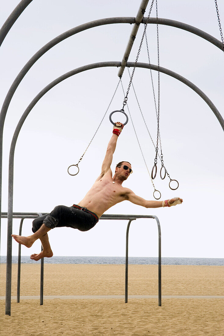 Caucasian man on the rings set, swinging from one ring to the next. Santa Monica Beach, Los Angeles, California.