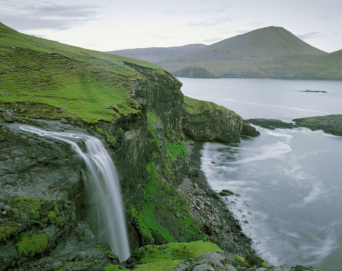 Waterfalls, mountain, green grass, sky. Faroe island. Denmark.